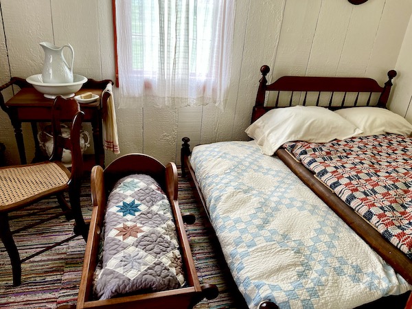 Adult bed, child's bed and cradle all with quilts at the Hoover home
