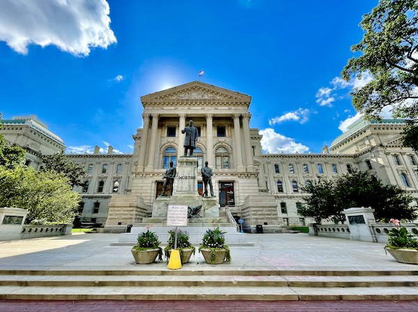 White Greek style building with bronze statues in front is the Indiana State Capitol in Indianapolis