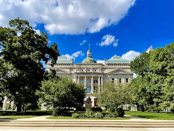 White statehouse building with columns and green roofs near Back Home Again mural at Indianapolis Speedway Indiana with Indy cars.