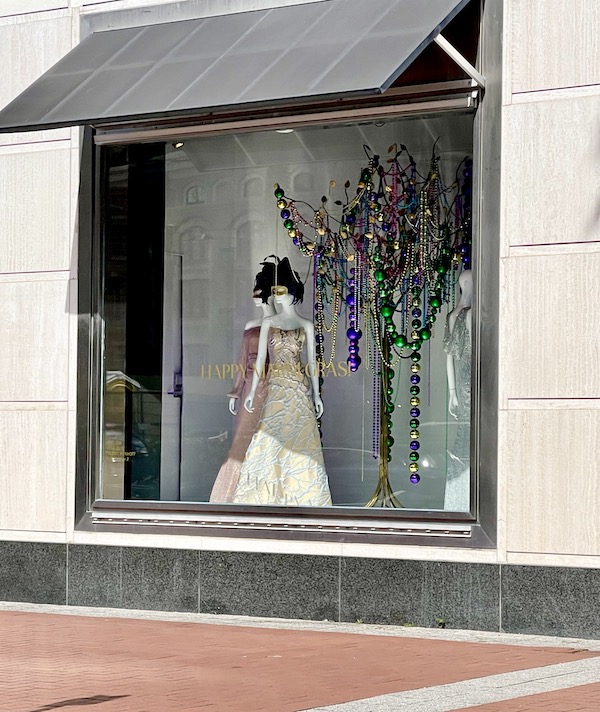 Store window with mannequin in gown and Mardi Gras decor.