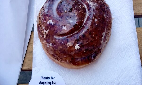 A glazed cinnamon roll on a white napkin sitting on a wood table at The Donut Bar Fort Wayne IN
