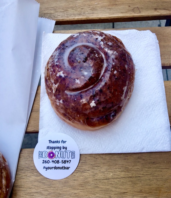 A glazed cinnamon roll on a white napkin sitting on a wood table at The Donut Bar Fort Wayne IN