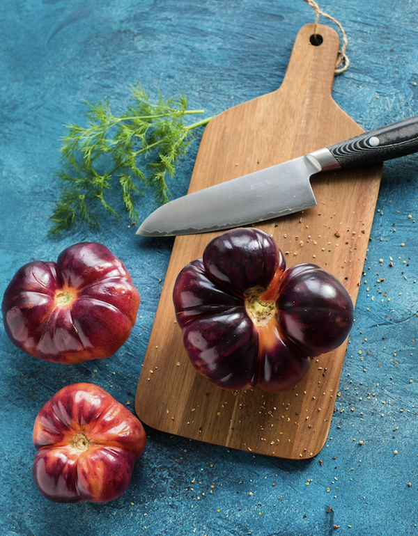 Cutting board with chef knife and heirloom tomatoes inspire e ways to improve your cooking skills today.