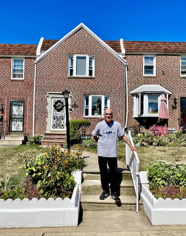Red brick row house with bay window, landscaping and Steve on the steps, one of All Our Houses in Northeastern America
