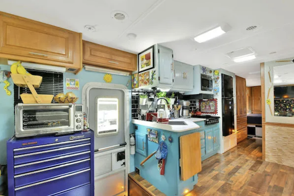 An RV kitchen with wood floor, teal and aqua cabinets and artwork from How to put the love back into cooking