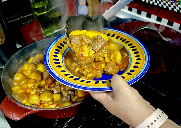 Ladling Alabama Style Beef Stew into a colorful bowl from a to on the stovetop.