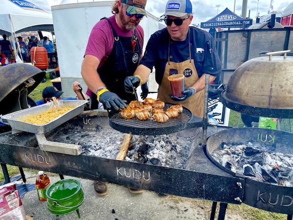 A two man team brushing BBQ sauce on bacon wrapped sausages at Hogs for the Cause