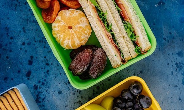 Green and yellow lunch boxes filled with sandwiches and fruit showing it's easy to Make Packing Lunch Quick and Easy