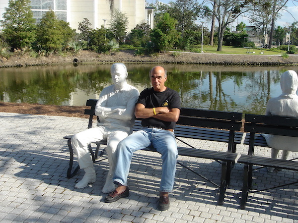 Steve sitting on a park bench mimicking the sculpture of a man sitting next to him.