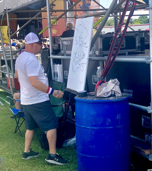 An artist painting a canvas as Buddy Guy performs at New Orleans Jazz and Heritage Festival