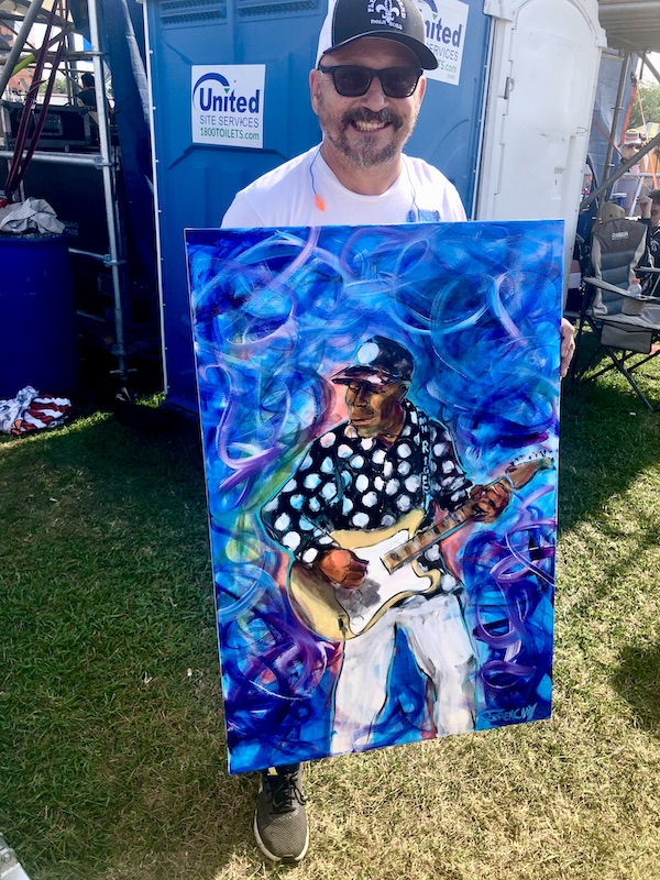 Artist showing off his finished painting of guitarist Buddy Guy at New Orleans Jazz and Heritage Festival