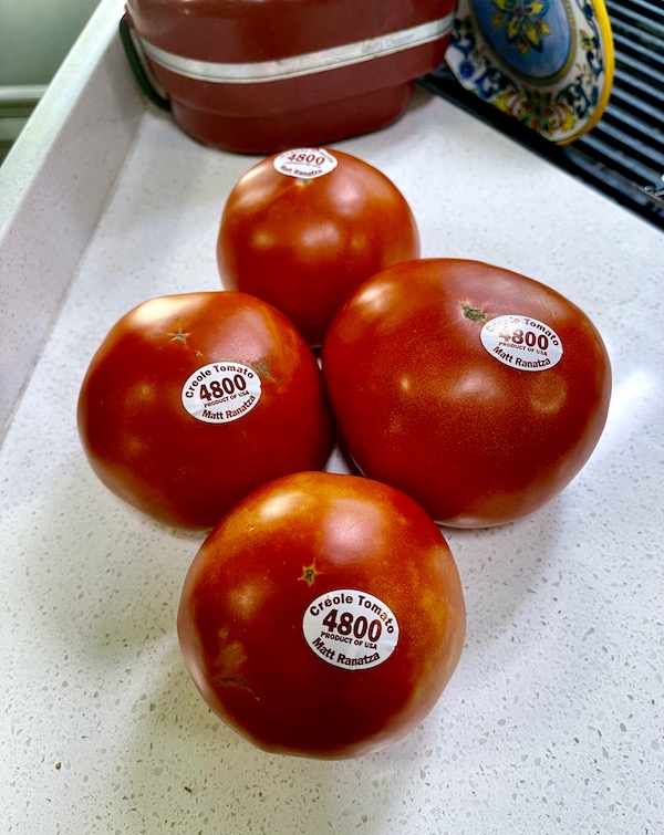4 perfect red tomatoes on a white counter purchased at the 37th Creole Tomato Festival NOLA
