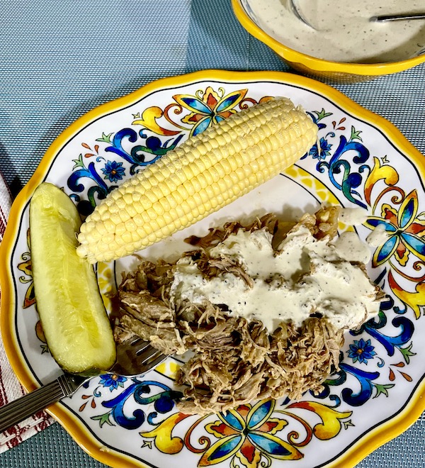 Colorful plate topped with Easy Alabama Pulled Pork, white sauce, ear of corn and pickle spear.