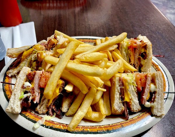 Plate topped with club sandwich cut in quarters and a mound of fries.