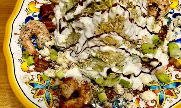 Dinner plate topped with The Wedge Salad Cajun Style sitting on a wood cutting board