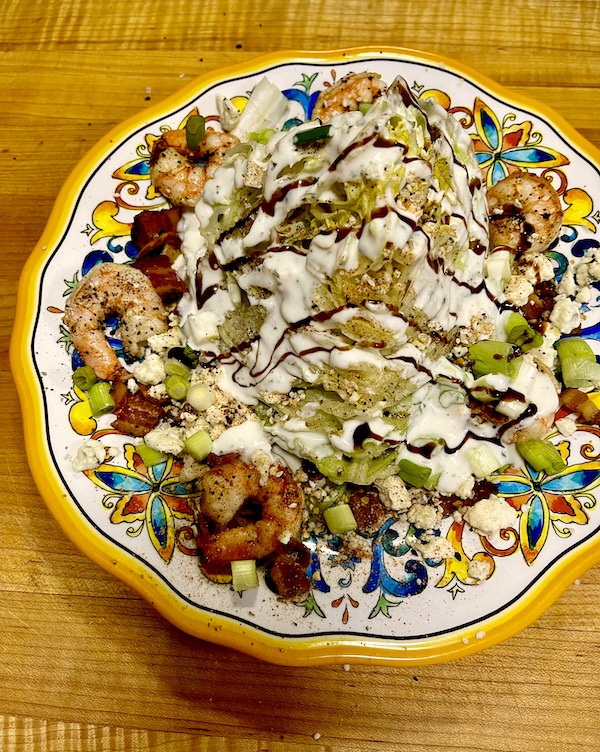 Dinner plate topped with The Wedge Salad Cajun Style sitting on a wood cutting board
