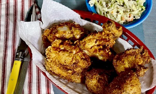 Basket of Southern Fried Chicken and dish of Buttermilk Coleslaw Perfect for Cookouts sitting next to a red and white striped napkin, fork and yellow handled knife.