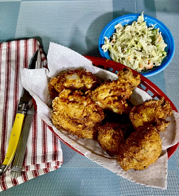 Basket of Southern Fried Chicken and dish of Buttermilk Coleslaw Perfect for Cookouts sitting next to a red and white striped napkin, fork and yellow handled knife.