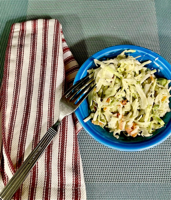 Small blue dish filled with Buttermilk Coleslaw Perfect for Cookouts and a fork with a red and white striped napkin next to the dish to the left.