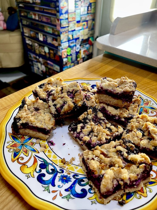Plate of Luscious Blueberry Lemon Bars on a plate sitting on a wood cutting board. Cobalt blue tool chest covered with magnets in the background.