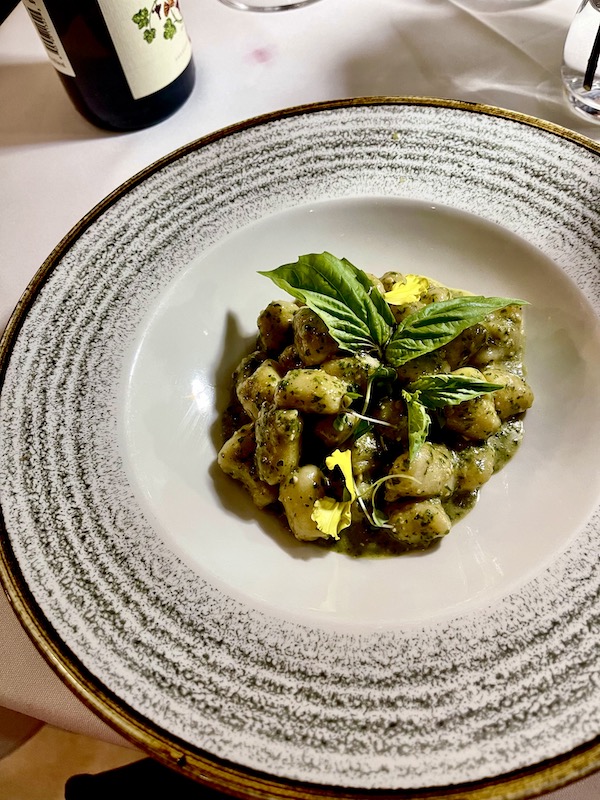 Large plate with portion of gnocchi with pesto sauce garnished with fresh basil leaves.