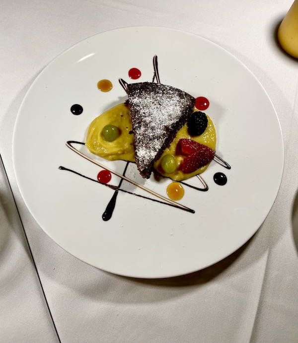 White plate topped with a wedge of chocolate cake, fruit, custard and chocolate creating a work of art from Pasta And... Margate Florida