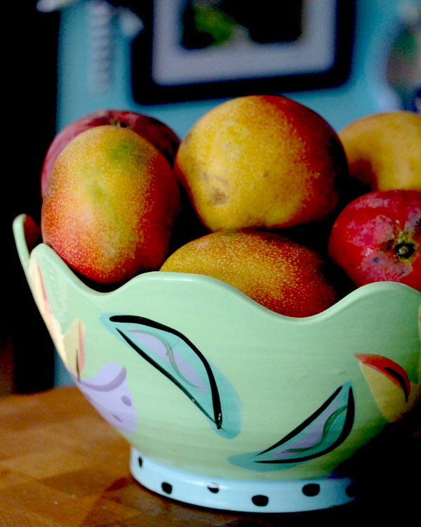 Aqua and pastel painted bowl filled with ripe mangoes
