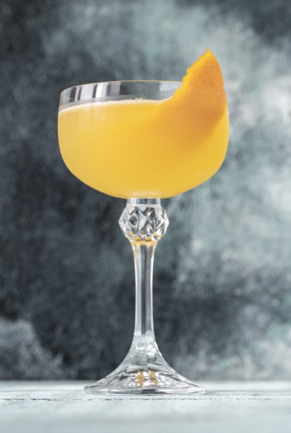 Stemmed wine glass filled with Tasting Arizona Chilled Mango Soup garnished with a wedge of mango.