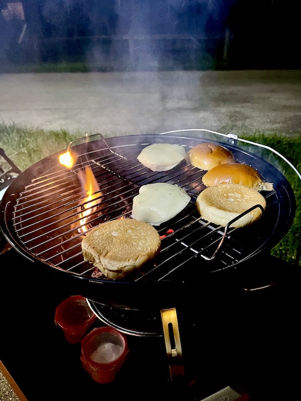 Burgers with cheese melting on top and buns toasting on the grill