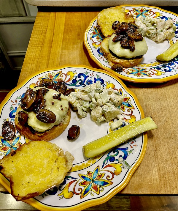 Two colorful plates topped with Mushroom Cheeseburgers, potato salad and a pickle spear