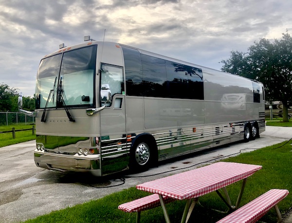 Grey motorcoach at an RV park with a picnic table in foreground.