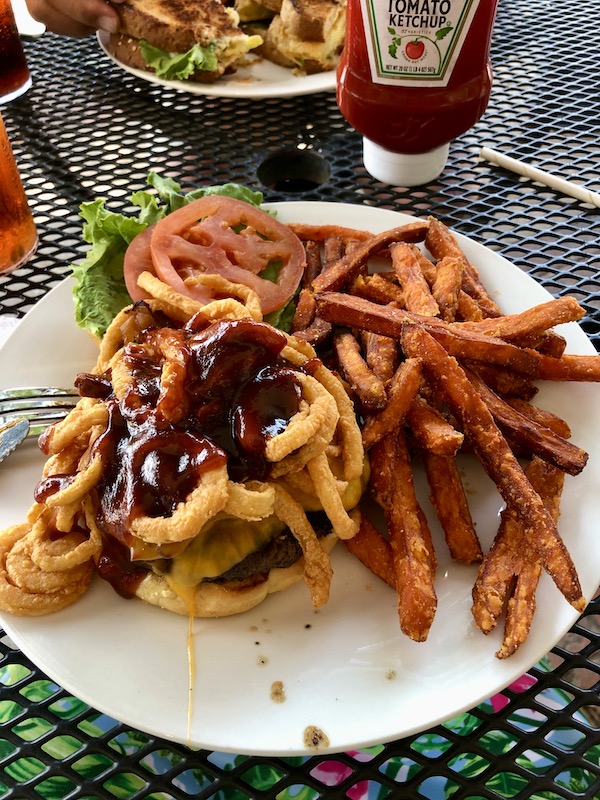 White plate topped with a burger, bbq sauce and onion rings with a side of fries. Part of my 3 Years RVing Year 1 Recap