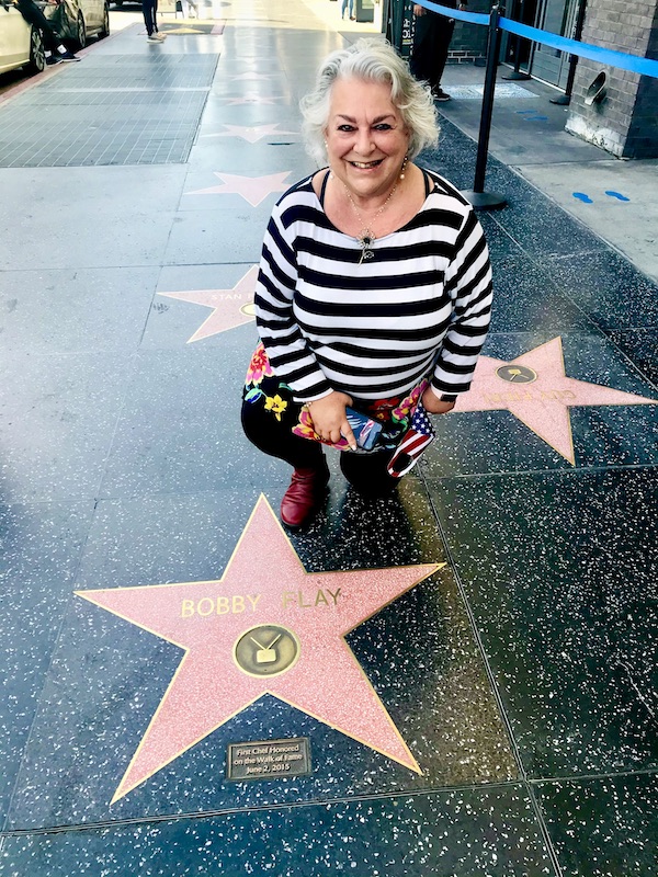 Me in a black and white striped top, kneeling by Bobby Flay's star on the Hollywood Walk of Fame.
