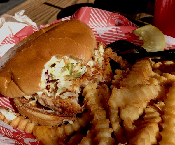 Basket lined with red and white deli paper, holding a spicy fried chicken sandwich with fries.