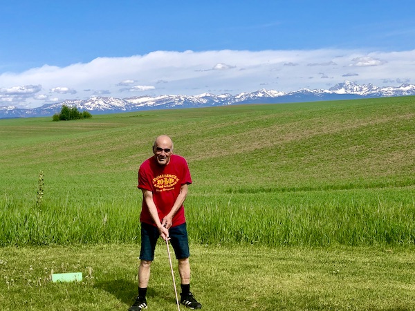 Steve about to hit a golf shot with mountains in the background. 3 Years RVing Year 3 Recap