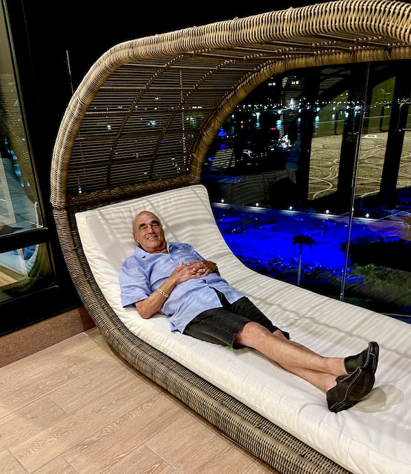 Man in blue shirt and black shorts lying on a rattan and white cushion chaise lounge after dinner at Elisabetta's Ristorante Bar Pizzeria