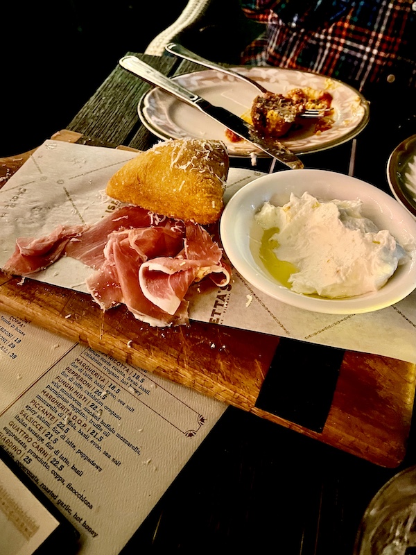 Wood cutting board toped with small bread, thin slices of ham and a white dish with ricotta at Elisabetta's Ristorante Bar Pizzeria 