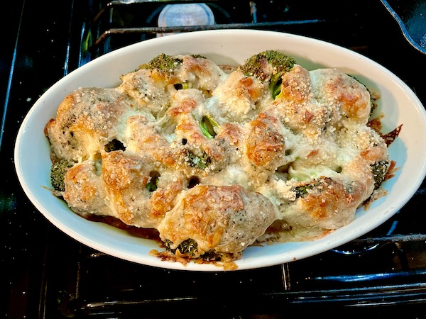 An white oval baking dish filled with golden brown Baked Broccoli Cheese Casserole resting on top of my gas stove in the RV.
