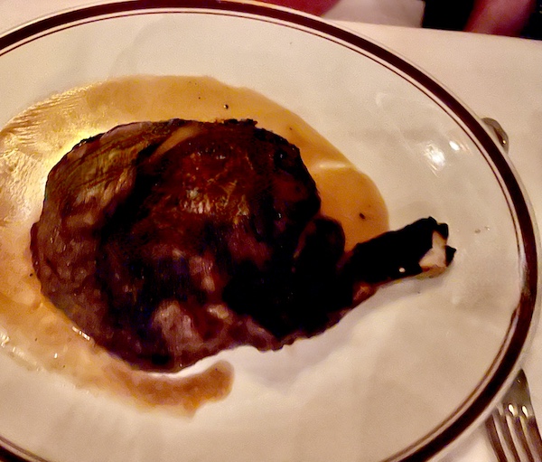 Black rimmed white plate topped with sauce and a huge bone in steak at Chops