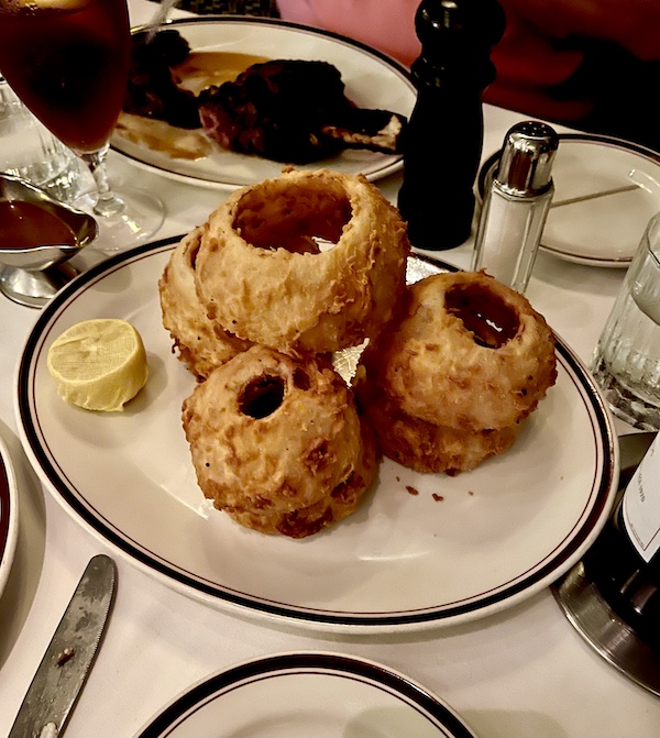 White plate topped with very very thick slices of fried onion rings and a sauce boat of steak sauce at Chops Lobster Bar Boca Raton
