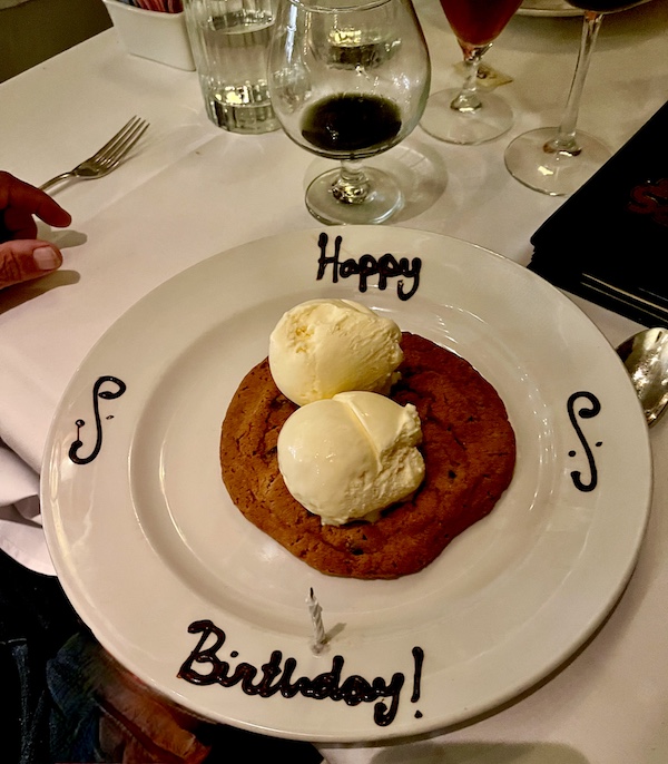 White plate with Happy Birthday written in chocolate on rim and topped with a large chocolate chip cookie and 2 scoops of vanilla ice cream at Chops Lobster Bar Boca Raton