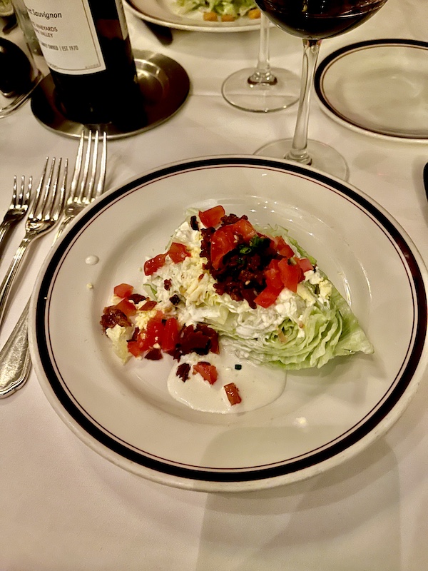Large salad plate topped with wedge of Iceberg lettuce, chopped tomato, bacon and blue cheese at Chops.