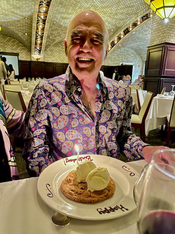 Steve in a blue paisley shirt about to blow out his birthday candle at Chops Lobster Bar Boca Raton
