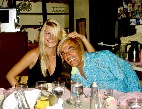 Steve in a turquoise shirt next to Eve in a black dress with Eve's blonde hair draped on his head.