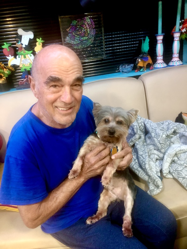 Steve in a blue T-shirt sitting on the sofa with our Yorkie Hershi on his lap.
