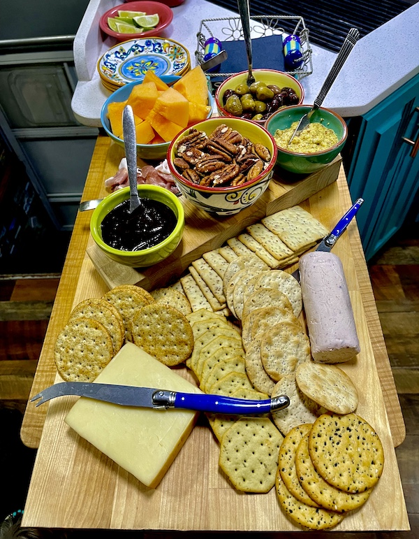 I Love to Feed People cheeses and salami and fruit on a wood cutting board.