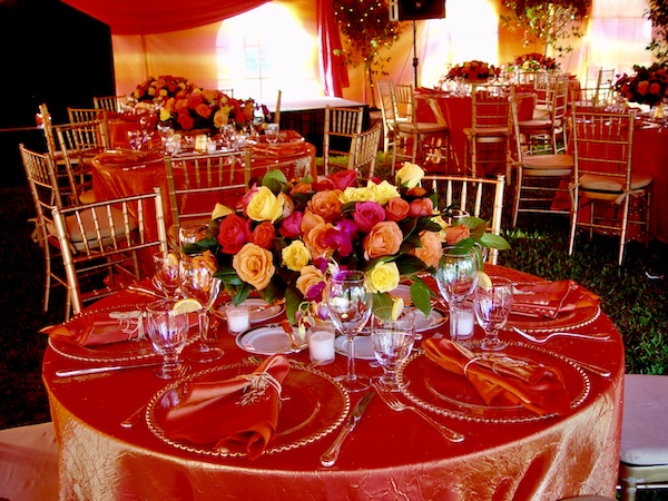 I Love to Feed People under a tent with shimmery orange tablecloth draped tables and colorful floral arrangements.