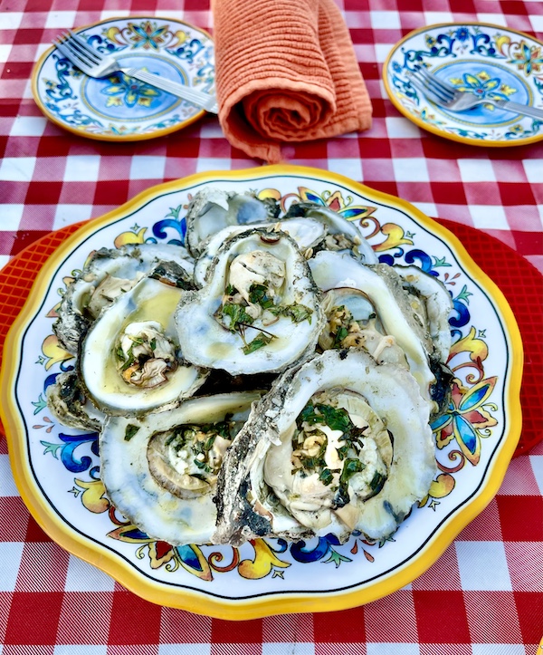 I Love to Feed People grilled oysters on a plate sitting on a red and white checkered tablecloth