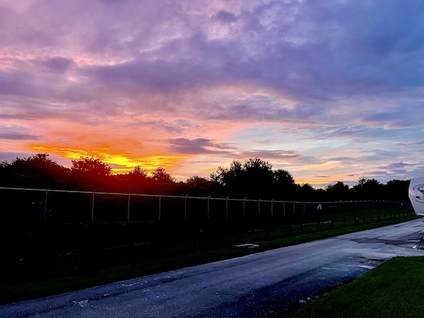 Setting sun creates sky of purple, pink, orange and yellow separated from the ground at John Prince Park Campground Lake Worth FL by a line of trees.