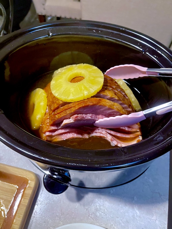 Small crock pot with spiral ham covered with pineapple rings.